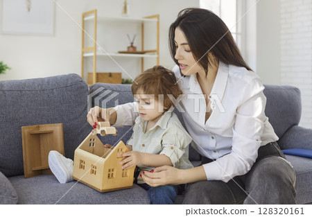 Mother, babysitter, little child playing with wooden toy house, having amusing game together, caring 128320161