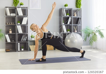 Home yoga workout of girl stretching, athlete standing in Twisted side angle pose on fitness mat 128320167