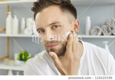 Man applying cream to face skin for healthy bathroom routine and skincare, fingers making smear 128320190