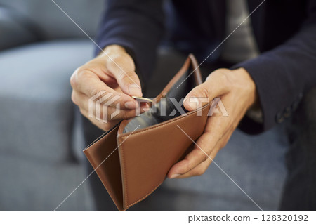 Man sitting on sofa at home wearing suit and putting coin into empty wallet. Man sitting on sofa at home wearing suit and putting coin into empty wallet. 128320192