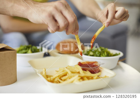 Man dipping French fries into ketchup to eat delicious potato sticks with spicy red sauce at home 128320195