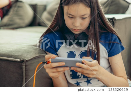 close up of Asian half-breed girl near green sofa using smartphone, headphones, home interior with soft light from window technology gadgets youth lifestyle close up of Asian half-breed girl near green sofa using smartphone, headphones, home interior with soft light from window technology gadgets youth lifestyle 128320629