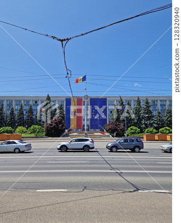 CHISINAU, MOLDOVA - JUNE 20, 2025 The Government House adorned with big EU and Moldovan flags on the facade and city traffic on the Stefan the Great avenue CHISINAU, MOLDOVA - JUNE 20, 2025 The Government House adorned with big EU and Moldovan flags on the facade and city traffic on the Stefan the Great avenue 128320940