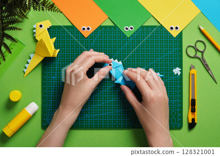 Making an origami dinosaur. Glue the eye to the head of the craft. Around us are items for paper crafts. Making an origami dinosaur. Glue the eye to the head of the craft. Around us are items for paper crafts. 128321001