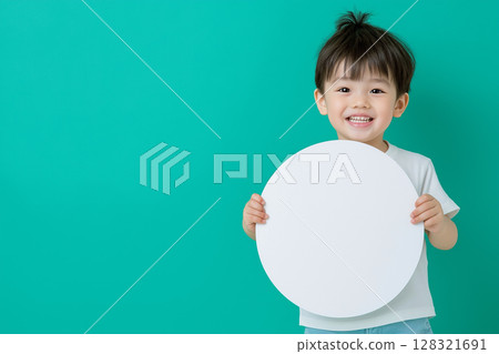 Child holding a blank circle on a green background, smiling and happy portrait of young boy 128321691