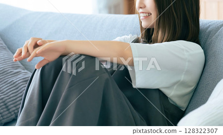 Smiling woman sitting on sofa in living room Smiling woman sitting on sofa in living room 128322307