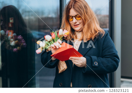Portrait of nice attractive lovely pretty cheerful woman getting receiving congrats card greetings and big bouquet flowers, outdoors 128323121