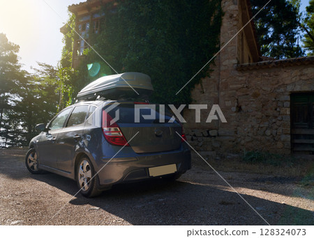 Compact Car Outdoors With Roof Cargo Box by Rustic Stone House at Sunset 128324073