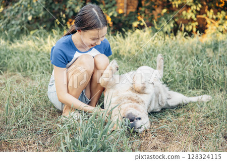 girl smiling petting dog lying on its back in grass backyard scene summer day peaceful atmosphere golden retriever enjoying attention concept of pet care animal shelter veterinary clinic 128324115