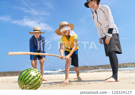 Family leisure scene enjoying watermelon splitting at the beach in summer 128324127