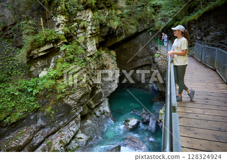 Stunning Young Woman Enjoying Scenic Mountain River View on a Hiking Trail in the Alps During Summer. Idyllic Alpine Landscape Captures the Essence of Outdoor Adventure and Natural Beauty. 128324924