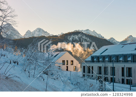 Beautiful alpine architecture in the snow during the golden hour, capturing a serene winter landscape with clear sky and sunny morning light, integrated harmoniously with the mountains. 128324998