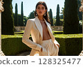 Elegant woman in a sophisticated suit posing outdoors in a formal garden 128325477