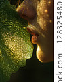 Close-up of a face illuminated by sunlight and a dewy leaf 128325480