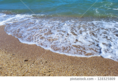 On a sunny summer day, the white, soft foam of the waves on a sandy beach by the sea On a sunny summer day, the white, soft foam of the waves on a sandy beach by the sea 128325809