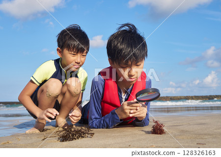 Elementary school students using magnifying glasses to observe nature on a summer beach 128326163