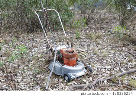 An old rusty lawn mower abandoned in a forest 128326234
