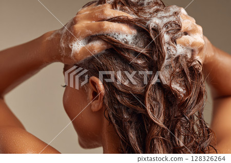 Back view of woman washing hair with shampoo, creating foam 128326264