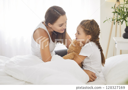 Cute little girl waking up in morning holding teddy bear tightly and talking sincerely to her mother 128327169