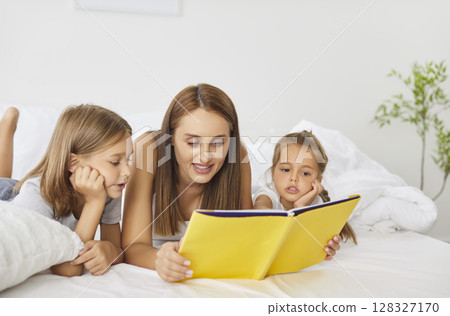 Happy family reading in bed, parents and cute small kids laughing lying together, children bonding  128327170