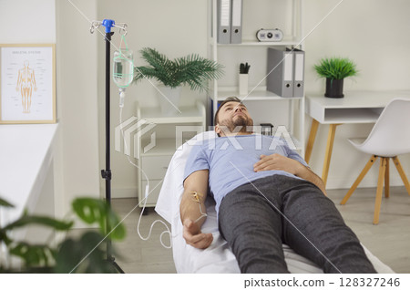 Sick adult man receiving IV drip infusion, lying on medical couch in clinic or hospital 128327246