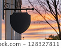 A Shield Shaped Sign Hangs Outside a Building Against a Beautiful Sunset Sky 128327811