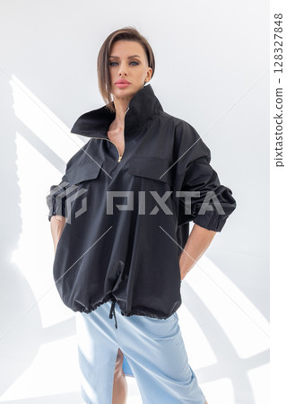 Elegant woman in black windbreaker jacket and light blue skirt on white background. Fashionable female style. Studio photography. Vertical photo. High quality photo 128327848