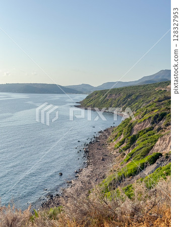 Stunning view of a rugged coastline with green cliffs and the expansive sea. The contrasting textures of rock and lush vegetation form a captivating natural landscape. Stunning view of a rugged coastline with green cliffs and the expansive sea. The contrasting textures of rock and lush vegetation form a captivating natural landscape. 128327953