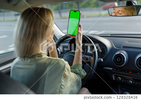 A woman in a vehicle gazing at her phone s green screen while possibly waiting or parked, showcasing the blend of technology in automotive environments and modern life dynamics A woman in a vehicle gazing at her phone s green screen while possibly waiting or parked, showcasing the blend of technology in automotive environments and modern life dynamics 128328416