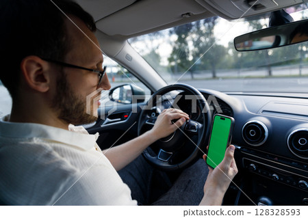 A Focused Individual Inside a Car Holds a Smartphone with a Green Screen While Preparing to Drive, Merging Technology with Modern Life 128328593