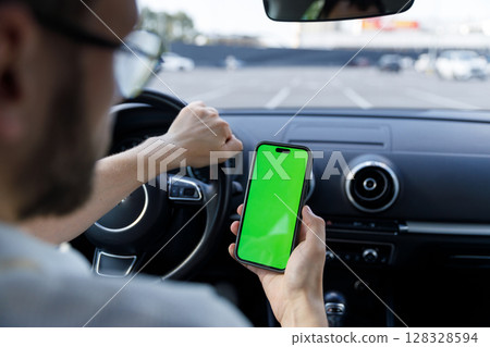 A Close-Up View of a Driver Holding a Smartphone with a Green Screen While Driving in an Empty Parking Lot 128328594