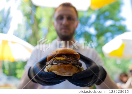 Delicious Gourmet Burger Featured in Outdoor Setting with Vibrant Greenery and Sunlit Atmosphere, Perfect for Food Lovers and Culinary Enthusiasts Seeking Flavorful Experiences. Delicious Gourmet Burger Featured in Outdoor Setting with Vibrant Greenery and Sunlit Atmosphere, Perfect for Food Lovers and Culinary Enthusiasts Seeking Flavorful Experiences. 128328615