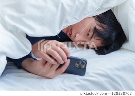 man using smartphone in bed 128328762