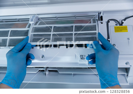 A Close-up View of Hands in Blue Gloves Carefully Removing the Filter from an Air Conditioning Unit for Maintenance and Cleaning to Ensure Efficient Performance and Air Quality 128328856