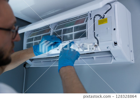 Professional Technician Performing Maintenance on a Split Air Conditioning Unit with Focus on Filter Replacement and Indoor Unit Care in a Residential Setting Professional Technician Performing Maintenance on a Split Air Conditioning Unit with Focus on Filter Replacement and Indoor Unit Care in a Residential Setting 128328864