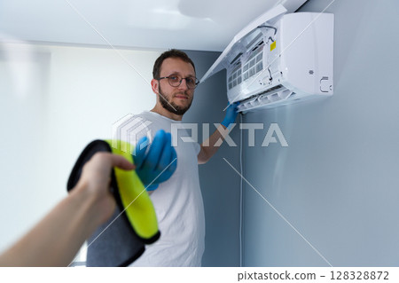 A Professional Male in Protective Gloves Working on an Air Conditioning Unit, Engaged in Maintenance at Home, Showcasing Cleanliness and Expertise for Comfortable Living Environments 128328872