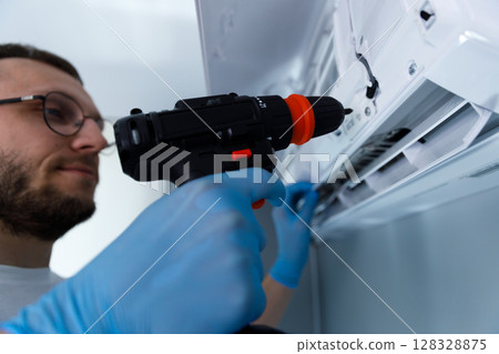 Expert Technician Performing Maintenance on an Air Conditioning Unit with a Power Drill for Efficient Service Excellence and Quality Assurance in Indoor Environments Expert Technician Performing Maintenance on an Air Conditioning Unit with a Power Drill for Efficient Service Excellence and Quality Assurance in Indoor Environments 128328875