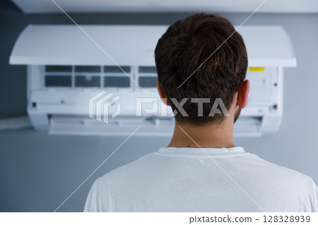 Man Observing Air Conditioning Unit While Standing in Room: A Detailed Focus on Indoor Climate Control and Its Importance in Modern Living Spaces for Comfort and Efficiency 128328939