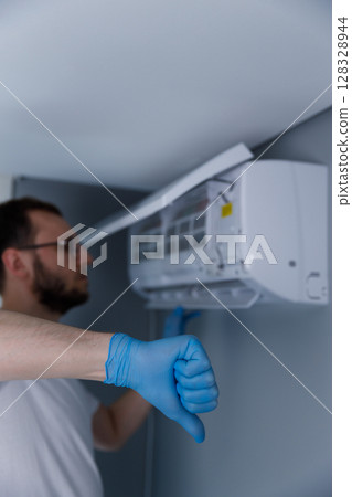 An Upset Technician Facing Air Conditioning Unit Issues While Wearing Gloves Signaling Disappointment with a Thumbs Down Gesture 128328944