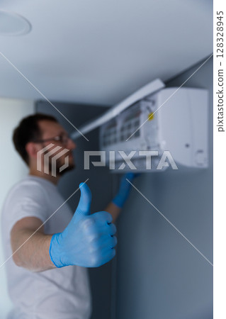 Professional Technician Giving Thumbs Up After Successfully Installing Air Conditioning Unit in Modern Indoor Setting, Showcasing Commitment to Quality and Comfort 128328945