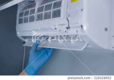 Expert demonstrates the maintenance of an air conditioning unit by removing its filter system designed for better airflow and cleanliness, showcasing proper hygiene practices and safety. Expert demonstrates the maintenance of an air conditioning unit by removing its filter system designed for better airflow and cleanliness, showcasing proper hygiene practices and safety. 128328952