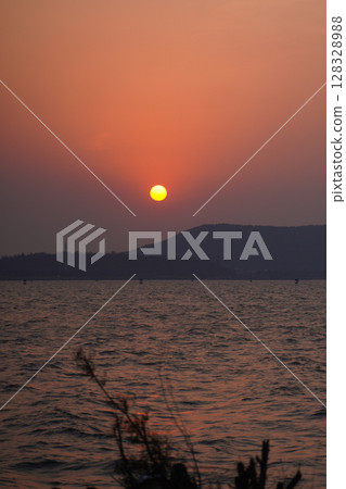 Breathtaking Sunset Over the Calm Waters with a Silhouette of Distant Mountains and Softly Rippling Waves Reflecting Warm Shades of the Setting Sun Breathtaking Sunset Over the Calm Waters with a Silhouette of Distant Mountains and Softly Rippling Waves Reflecting Warm Shades of the Setting Sun 128328988