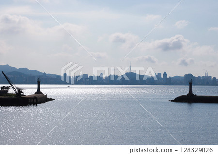 Stunning Coastal View Featuring Lighthouses and City Skyline Under a Bright Sky with Rolling Clouds and Shimmering Water Surface - A Perfect Representation of Urban and Natural Harmony Stunning Coastal View Featuring Lighthouses and City Skyline Under a Bright Sky with Rolling Clouds and Shimmering Water Surface - A Perfect Representation of Urban and Natural Harmony 128329026