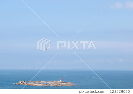 A Serene Coastal Landscape Featuring a Striking Lighthouse on a Rocky Island Surrounded by Expansive Ocean Waters and a Clear Blue Sky 128329030
