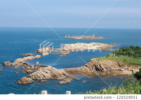 Stunning Coastal View Featuring Rocky Outcrops and a Lighthouse Against a Clear Blue Sky and Serene Ocean Landscape Stunning Coastal View Featuring Rocky Outcrops and a Lighthouse Against a Clear Blue Sky and Serene Ocean Landscape 128329031