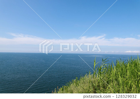 Majestic Coastal View: Endless Blue Ocean Meets Bright Sky Over Lush Green Grass On The Clifftop, Inviting Serenity And Peaceful Moments In Nature's Embrace Majestic Coastal View: Endless Blue Ocean Meets Bright Sky Over Lush Green Grass On The Clifftop, Inviting Serenity And Peaceful Moments In Nature's Embrace 128329032