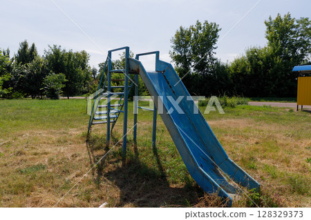 A Vibrant Blue Slide in a City Park Surrounded by Greenery Inviting Joy and Playfulness for Children and Families Enjoying the Outdoors on a Sunny Day 128329373