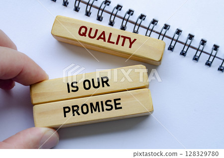 Quality Is Our Promise text on wooden blocks over notebook conveys commitment backed by meaningful intent 128329780