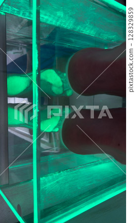 A Fascinating Display of Reflexology in a Green Gel-filled Container with Feet Immersed for Spa Therapy and Relaxation, Showcasing the Unique Treatment Experience 128329859