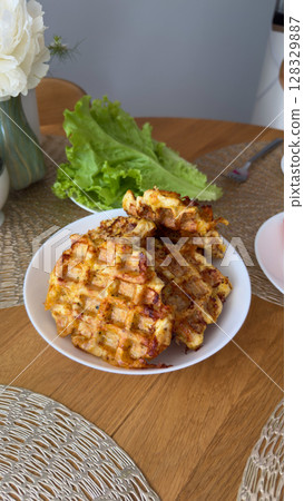 Delicious Homemade Savory Waffles Served on a White Plate at a Beautiful Table Setting with Fresh Green Lettuce and Flowers in a Charming Indoor Space 128329887